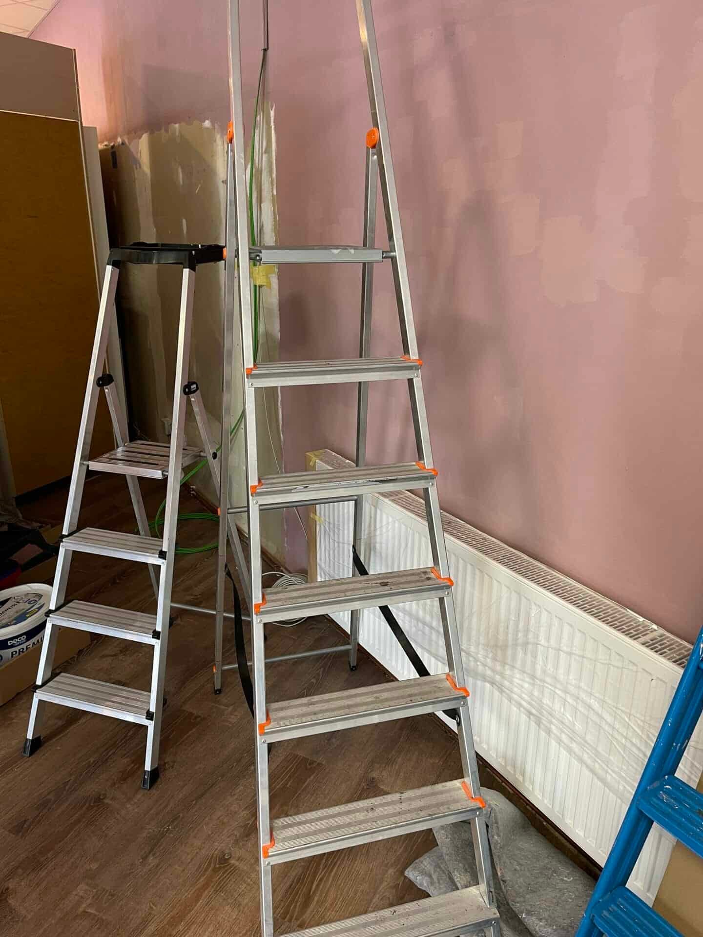 Eine Leiter in einem Raum mit einer rosa Wand.